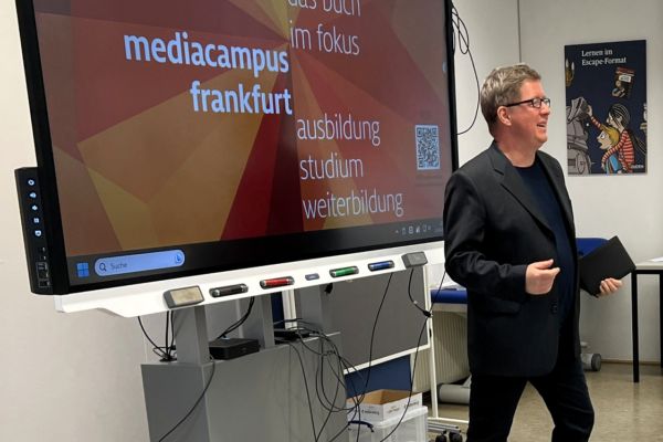 Patrick Musial neben einer digitalen Tafel im Klassenraum am mediacampus in Frankfurt.